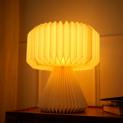 A white origami paper table lamp with a pleated design, close view with warm ambient light