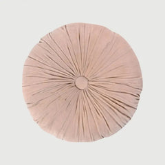A round, light pink plush cushion with a central button and radiating pleated details, shown against a solid light gray background.