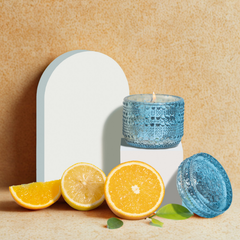 Orange Cassis Fragrance Trinket Jar Candle, aqua glass jar and lid styled with citrus on a sand-textured backdrop