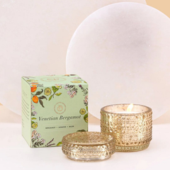 Venetian Bergamot Fragrance with Trinket Jar Candle, lit gold glass jar, lid and green box against a white stone disc
