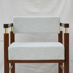 A mid-century modern armchair with a light gray textured linen seat and back cushions, supported by a dark brown wooden frame with gold metal accents.