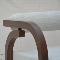 Close-up of a wooden armchair with a curved dark brown frame and a light beige textured fabric cushion.