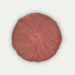 A round, dusty rose velvet floor cushion with a gathered, pleated design and a small gold tag on the right edge, shown against a light off-white background.