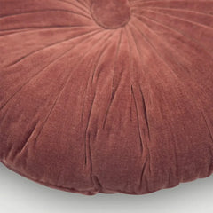A close-up of a round, tufted pouf or floor cushion in a dusty rose velvet fabric, showing the textured fabric and radial stitching details.