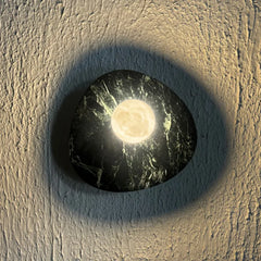 Round Aureole Green Textured Wall Sconce in alabaster stone base fixture with a glowing moon design in the center, mounted on a textured beige plaster wall.