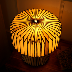A white origami paper table lamp with a pleated design, warm ambient light, top view.