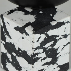 A close-up of a decorative cube-shaped box with black and white pattern, topped with a smooth black rounded bowl on a light gray background.