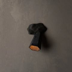 A modern wall sconce with a dark textured rock-like top and a faceted geometric shade, casting a warm light against a textured gray wall.