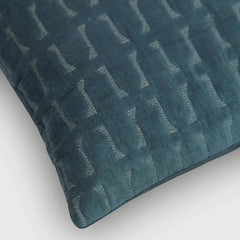 A close-up of a dark teal textured throw pillow with a woven geometric pattern, shown on a clean white background.