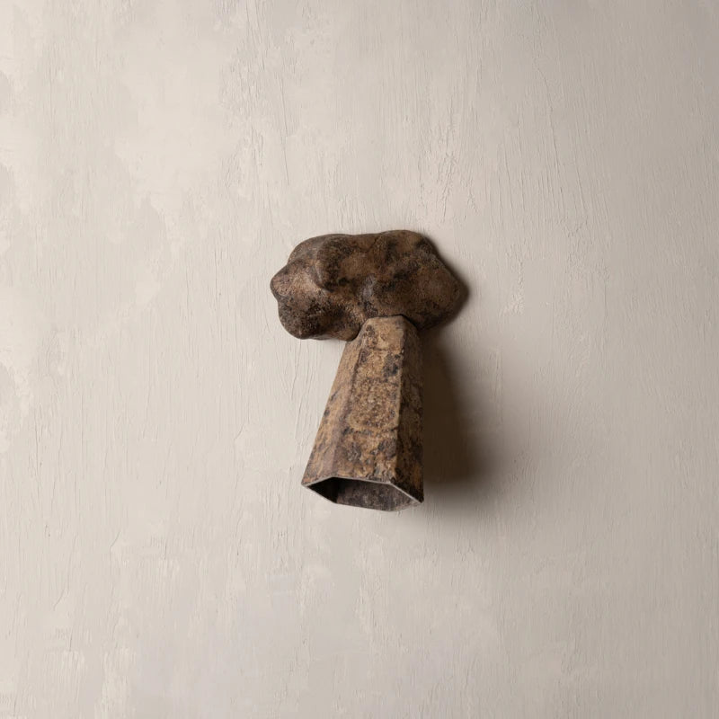A rustic metal wall sconce with a textured, weathered bronze-brown finish, mounted on a light beige plaster wall.