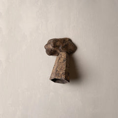 A rustic metal wall sconce with a textured, weathered bronze-brown finish, mounted on a light beige plaster wall.