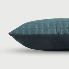 A close-up of a dark teal throw pillow with a subtle textured geometric pattern on the top half and a solid dark navy bottom half, set against a light gray background.