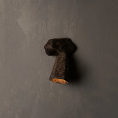 A rustic, dark brown textured wall sconce light fixture mounted on a gray textured wall, casting a warm glow downwards.