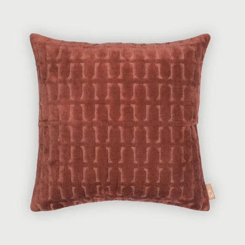 A square throw pillow in a textured rust-brown velvet fabric with a raised geometric pattern, shown against a light gray background.