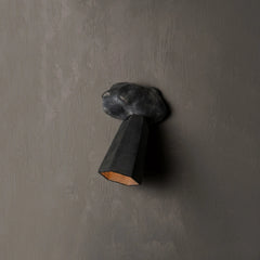 A sculptural black metal wall sconce with a textured cloud-like shade and a faceted cone-shaped shade, mounted on a textured gray wall.