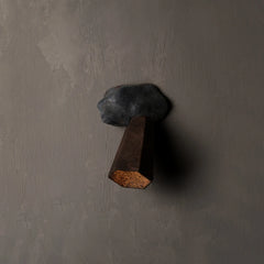 A rustic wall-mounted hook shaped like a dark gray stone with a brown wooden peg, set against a textured gray plaster wall.
