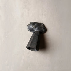 A dark gray, sculptural wall-mounted light fixture with a textured, cloud-like top and a faceted cone-shaped shade, mounted on a textured beige plaster wall.