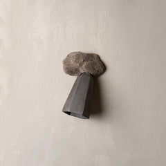 A sculptural wall-mounted light fixture with a textured gray concrete cloud-like top and a dark gray geometric cone-shaped shade, mounted on a textured beige plaster wall.
