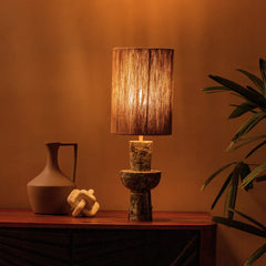 Natura Table Lamp with a textured base and brown shade on a wooden surface, with warm ambient light