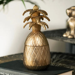 Gold pineapple-shaped candle votive on a surface with a blurred background