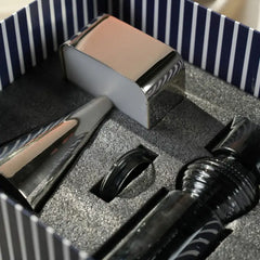 A close-up of a gift boxed set containing polished metallic portable table lamp with dark ribbed Glass Carafe arranged in a gray foam insert inside a navy-and-white striped box.