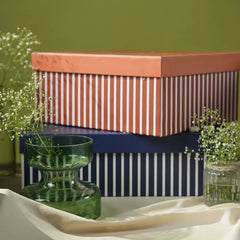 A stack of decorative gift boxes with striped patterns, styled with green glass vases, Votive & Wax Tablet