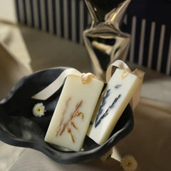 Two rectangular Wax Tablets with dried botanical inclusions, tied with white ribbons and displayed in a dark ceramic dish.