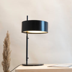 Svelte Scandi Table Lamp featuring a slender stem and a circular mounting base with a black shade casting warm light.