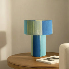 Multicolored cylindrical table lamp on a wooden surface with a neutral background