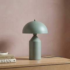 Green Cone Pagen Table Lamp on a wooden surface with a pinkish-brown background