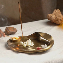 Taral Puja Thaali diya being lit with a matchstick beside jasmine and incense on white cloth, antique brass finish