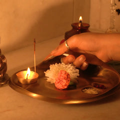 Taral Puja Thaali with lit diya and flower offering placed by hand on home altar, antique brass finish, side view