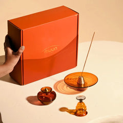 Kalash Oil Lamp + Incense Holder + Small Bell in amber glass beside orange Muun gift box held in hand