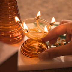 Glass Short Diya, hand beside lit short diya with clear bowl and amber base