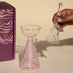 Glass Tall Diya & Ringing Bell Pink- hand holding clear glass bell beside ribbed pink borosilicate diya