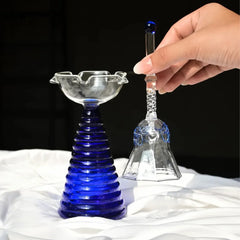 Glass Tall Diya & Ringing Bell Blue, hand holding glass bell with blue Om detail beside diya on white fabric