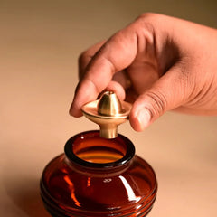 Kalash Oil Lamp + Small Ringing Bell, hand lifting gold-tone cap off amber glass kalash lamp