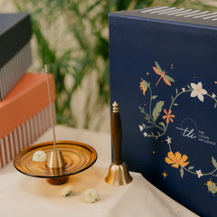 A dark blue gift box with floral illustrations and the brand name 'the living influence', alongside a brass incense holder and brass wooden-bell . 