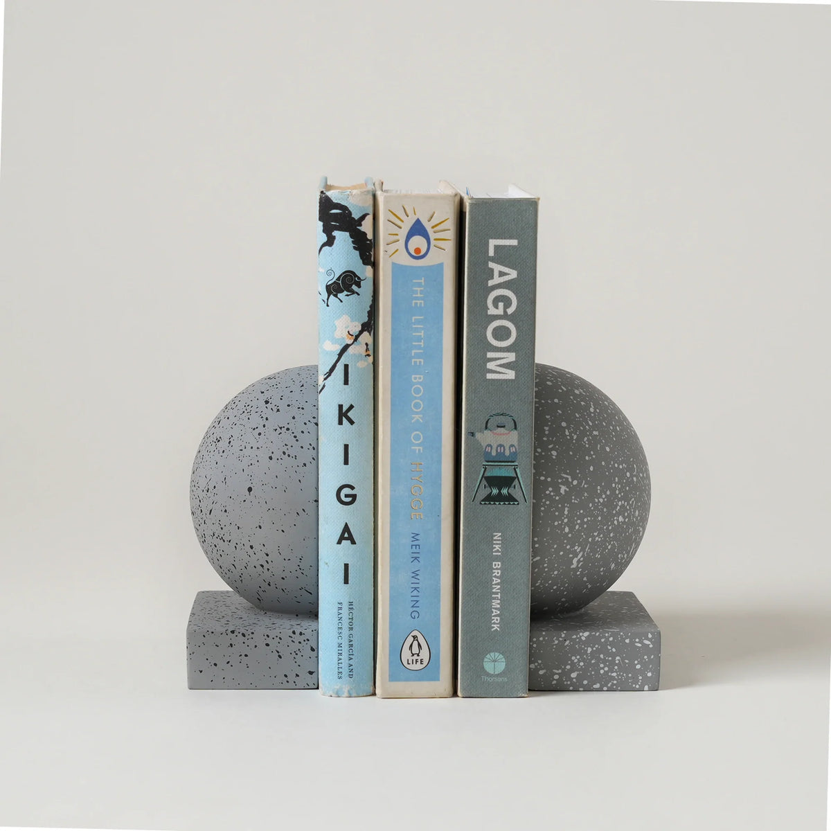 Monolith Concrete Bookends holding three books on a light gray background