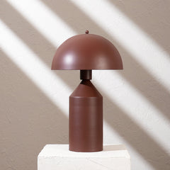 Brown table lamp made of iron on a white pedestal against a beige wall with shadow patterns