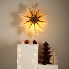 A wall mounted, Snowflake Flower Festive origami lampshade light with a warm glow, placed above decorative items