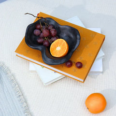 Black decorative organic bowl with fruits on a stack of books.