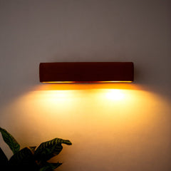Wall-mounted light fixture casting a warm glow on a plain wall with a plant in the corner.