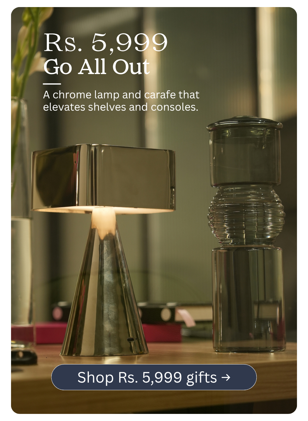 Promotional graphic for a home decor bundle featuring a modern chrome table lamp and a dark gray glass carafe, with text reading 'Rs. 5,999 Go All Out'.