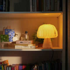 Mushroom Origami Table Lamp is placed on shelf next to room spray and books.