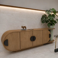 A modern curved wooden sideboard cabinet with dark round door handles, styled in a minimalist room with a potted monstera plant and a small elephant figurine on top.