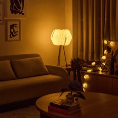 Lifo floor lamp with a beige origami-inspired linen shade switched on showing warm ambient glow 