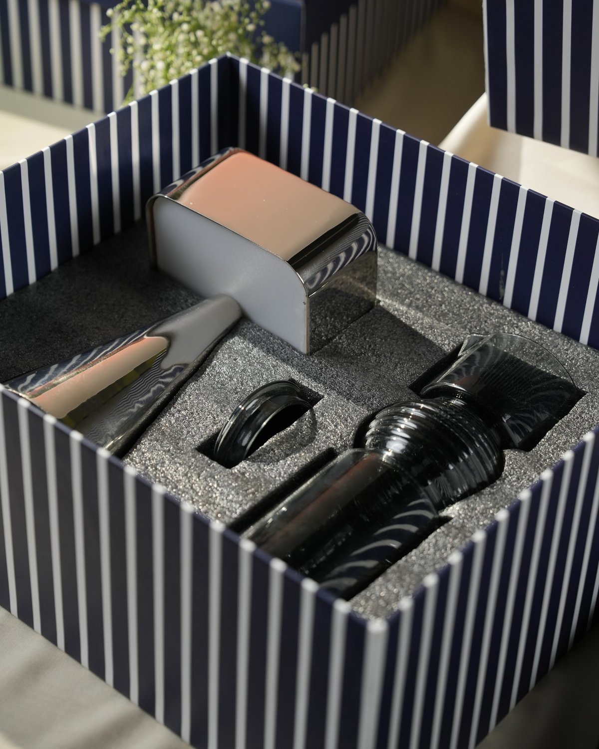A luxury gift set in a navy and white striped box, containing a silver metallic chrome portable lamp and hand-blown Coil Glass Carafe