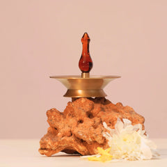 Baby Vilakku Oil Lamp resting on a natural rock with white flower, brass saucer and amber glass finial