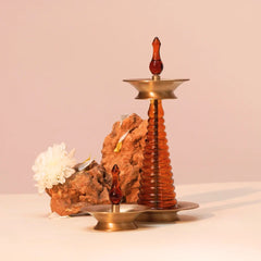Nilavilakku Oil Lamp with smaller brass and amber glass lamp, styled with rock and white flower, side view